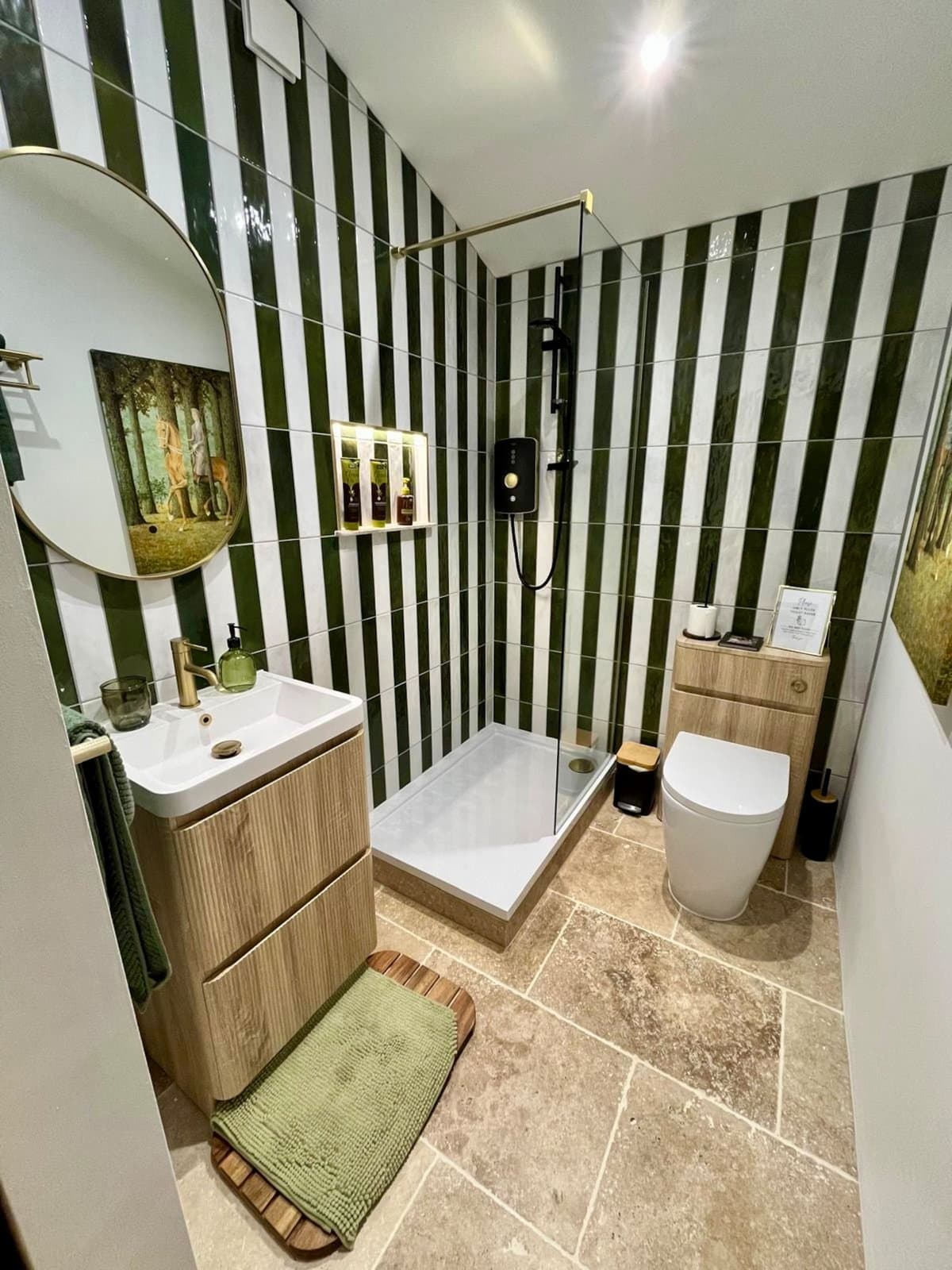 The shower room, with green and white striped tiles, a round mirror and an oak vanity
